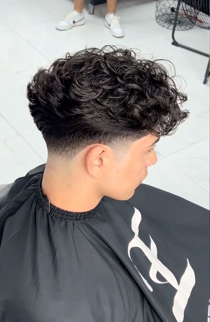 A dark curly taper fade with a clean neckline