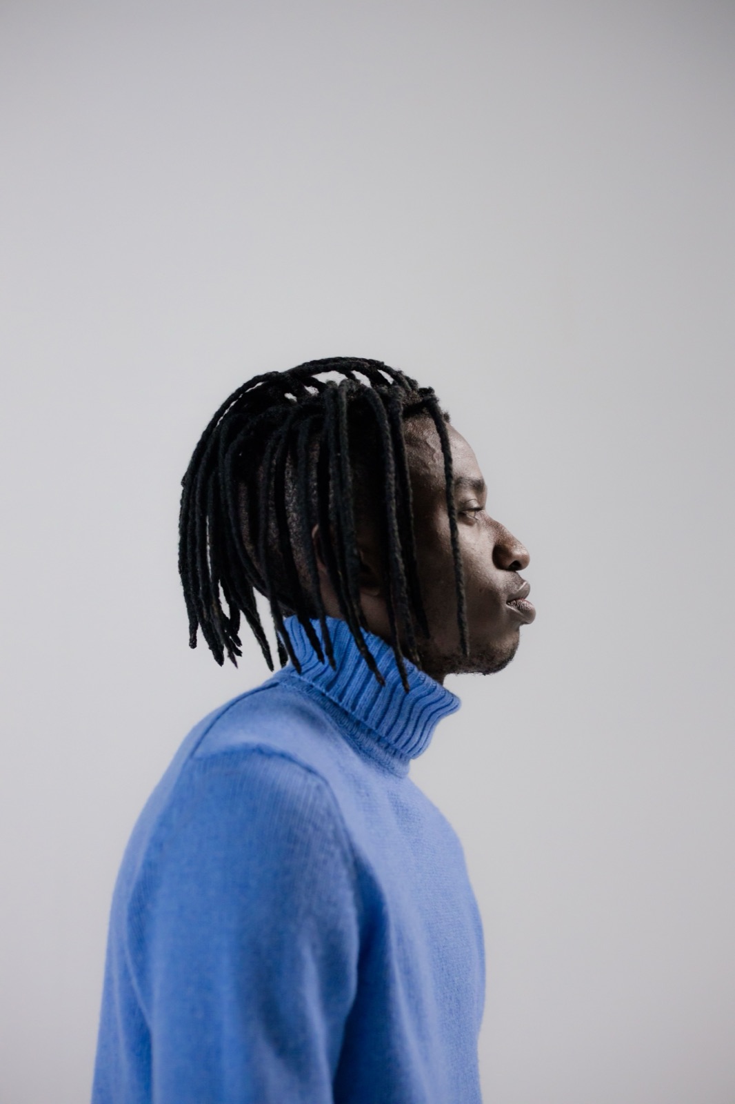 A clean side profile of dreads over a blue sweater