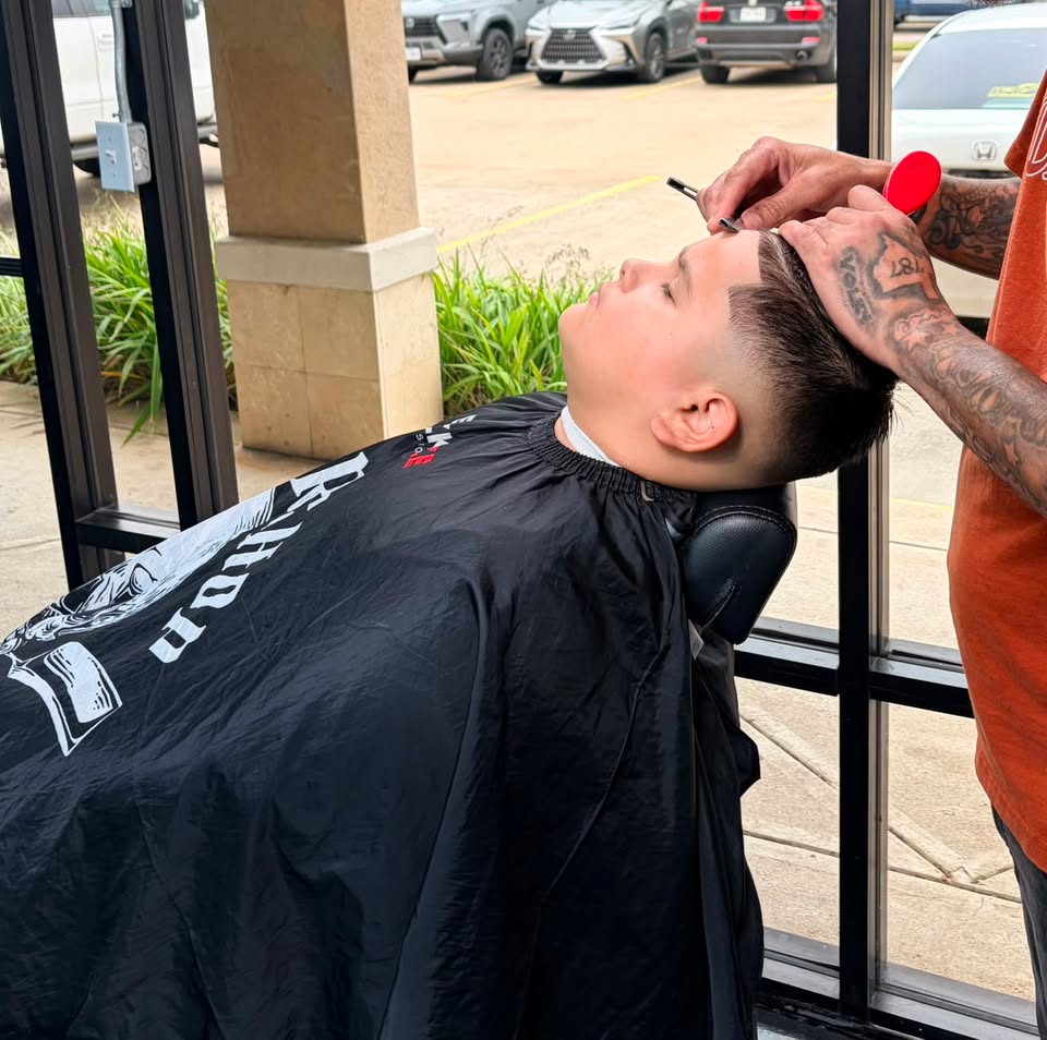 A barber lining up a client's hairline outside the shop